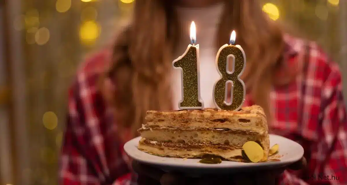 A képen egy sütemény látható, amelyet két égő gyertya díszít, a gyertyák száma "18". A sütemény egy szeletelt torta, amelyet egy fehér tányéron tartanak. A háttér homályos, de láthatóan egy ünnepi hangulatot sugall, a háttérben látható személy piros kockás inget visel.